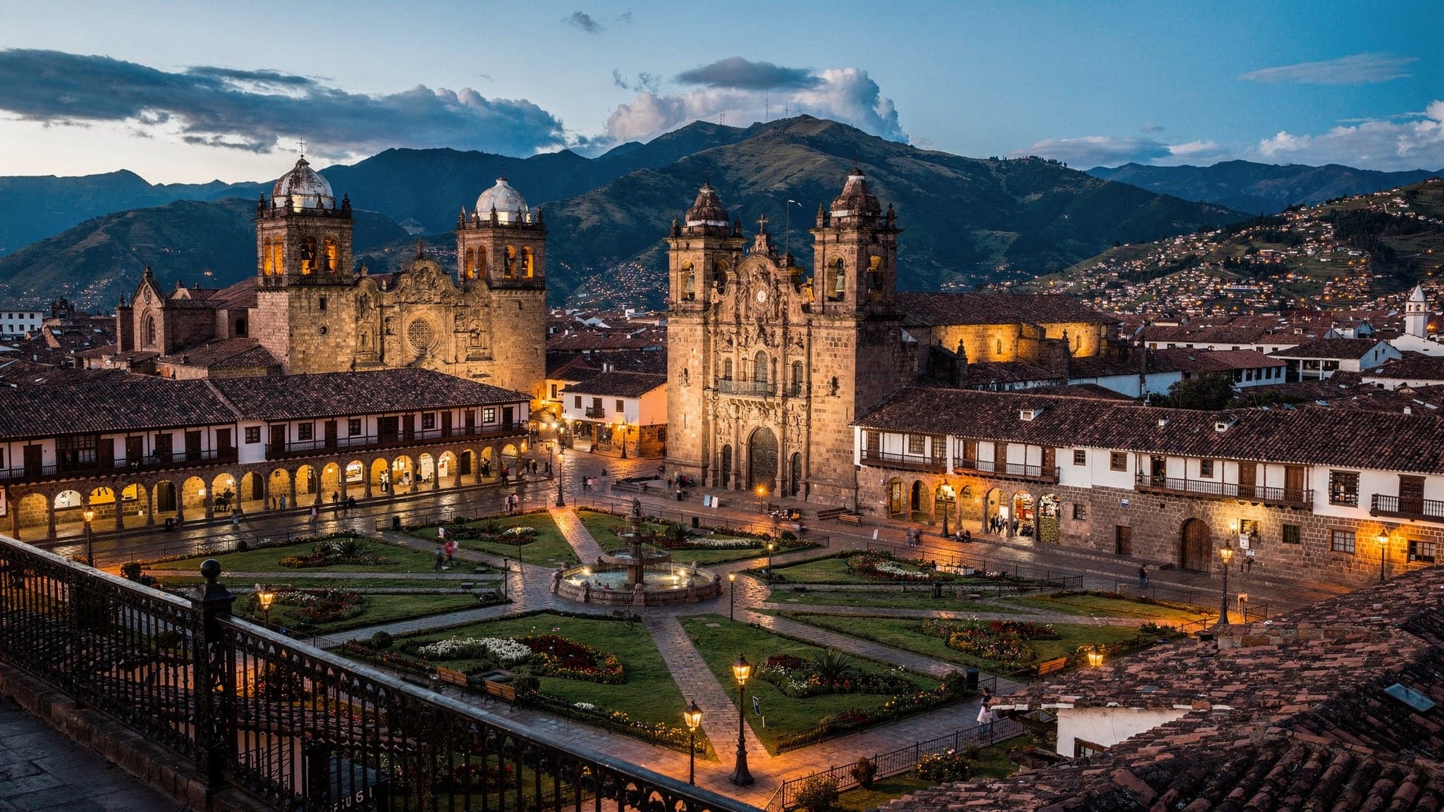 Cusco's Plaza de Armas at blue hour, with the floodlit cathedral and La Compañía church below terracotta rooftops and dark Andean ridges