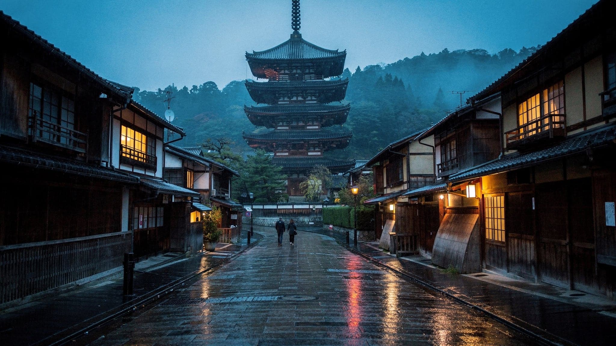 The five-storey Yasaka Pagoda rising above the wet stone slope of Yasaka-dori in Higashiyama at blue hour, wooden townhouses with lit windows below