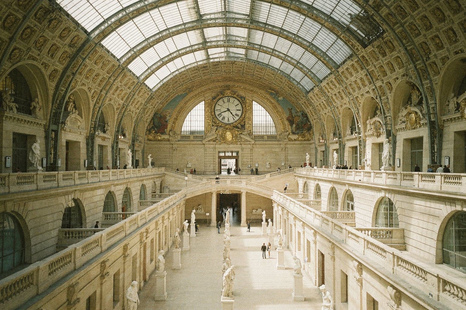 The gilded clock above rows of white marble sculptures in the nave of the Musée d'Orsay, a former railway station