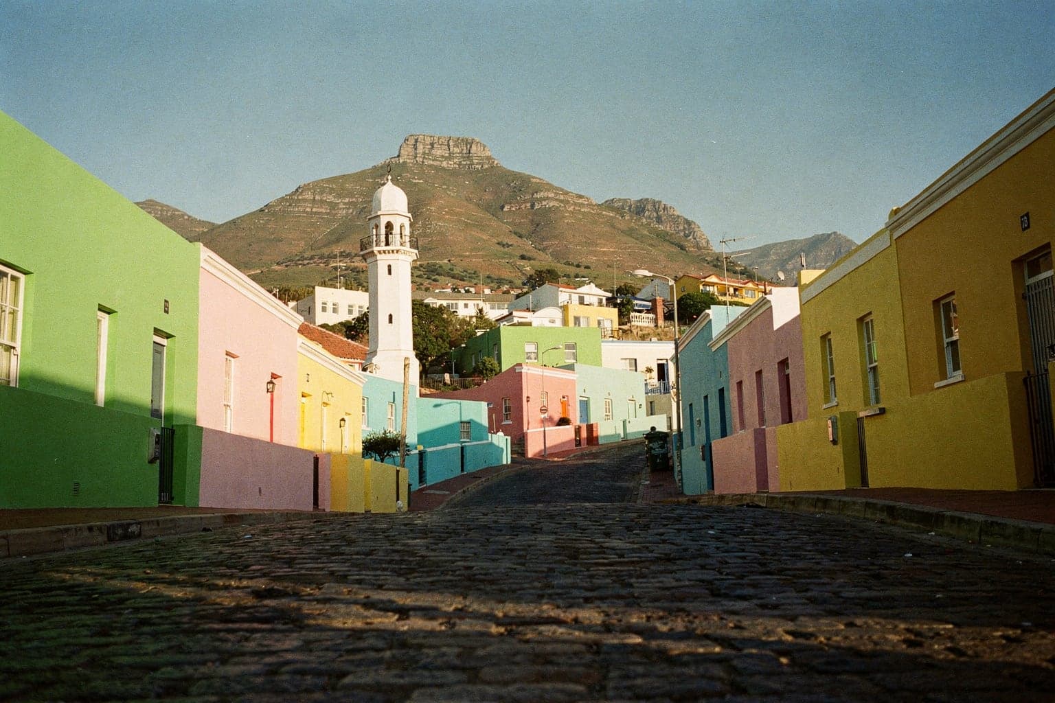Brightly painted Cape Malay houses on a steep cobbled Bo-Kaap street with a minaret and Signal Hill behind