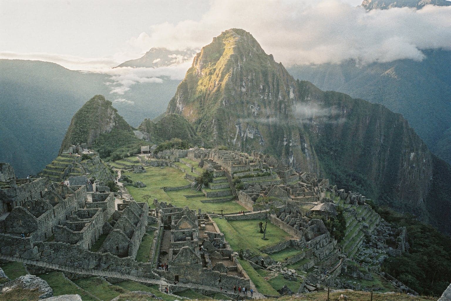 Machu Picchu's stone citadel in early light with Huayna Picchu behind and cloud lifting from the gorge