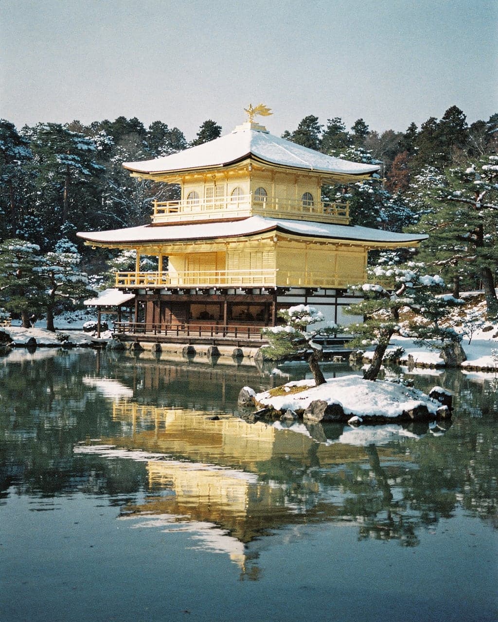 Kinkaku-ji's gold-leafed pavilion reflected in its pond on a clear winter morning, snow on the roof and pines