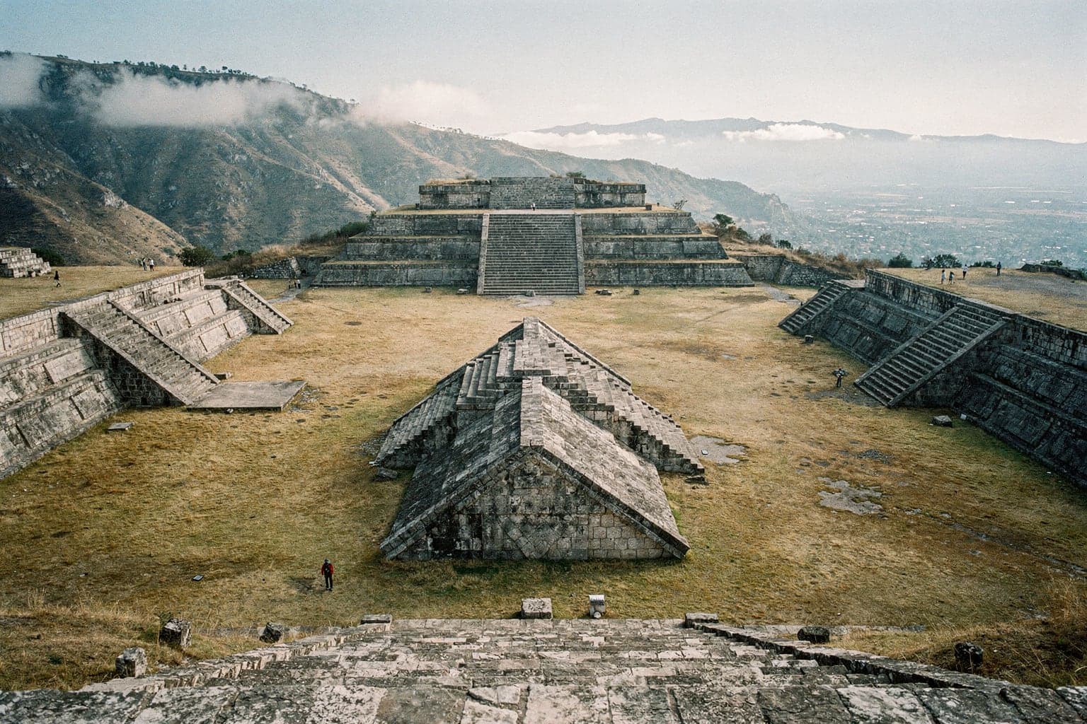 The Gran Plaza of Monte Albán in early morning light, with stone platforms and stairways and the Oaxaca valley and mountain ridges beyond
