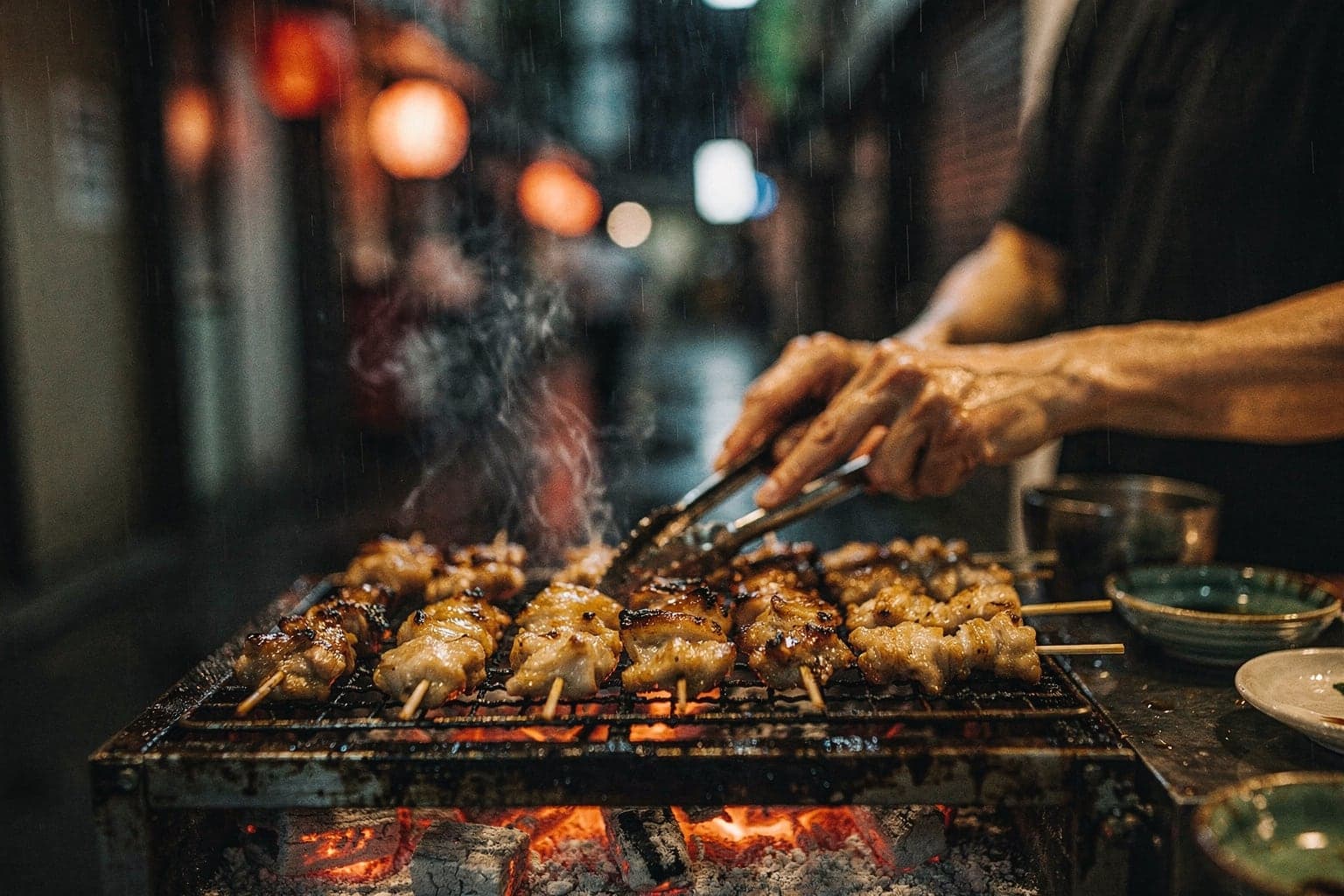 A narrow alley of tiny yakitori bars in Shinjuku's Omoide Yokocho at night, red lanterns and grill smoke over wet paving